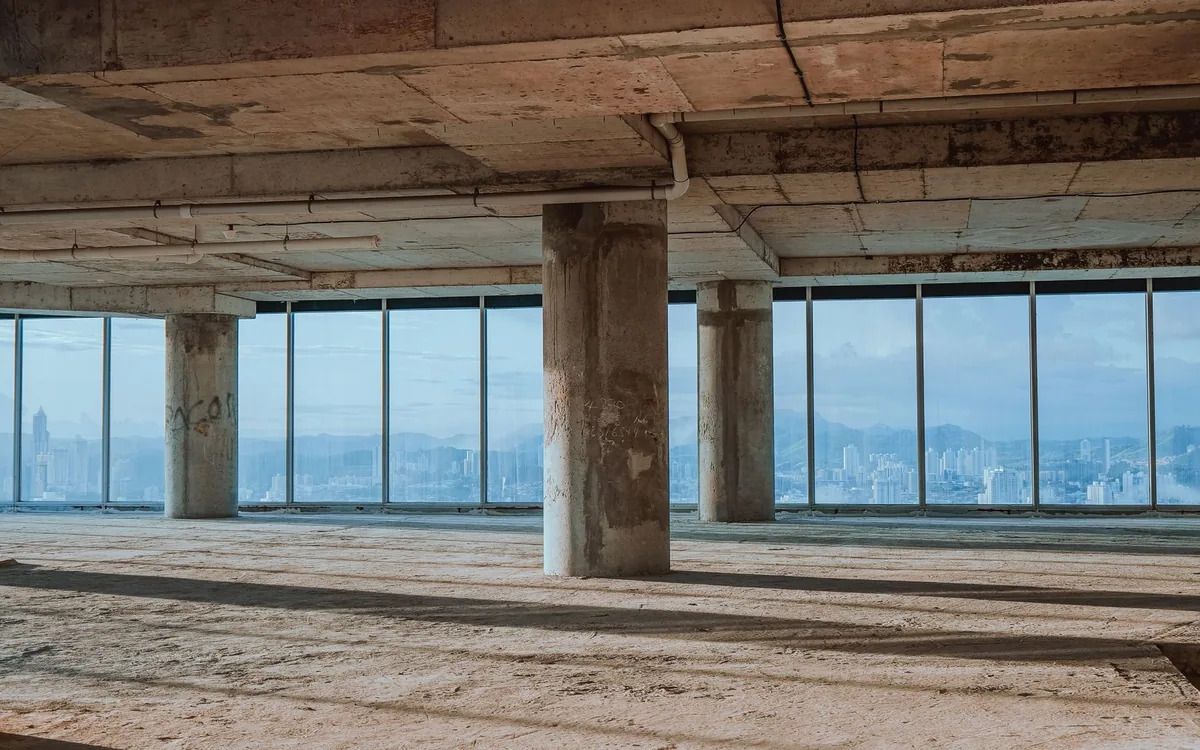 Salão comercial amplo e vazio com colunas de concreto e janelas ao fundo.