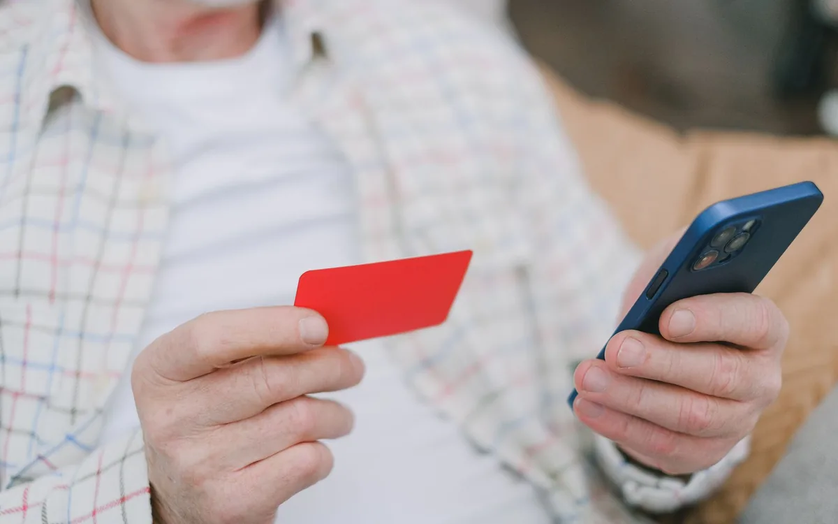 Mãos de uma pessoa segurando um cartão vermelho e um celular.