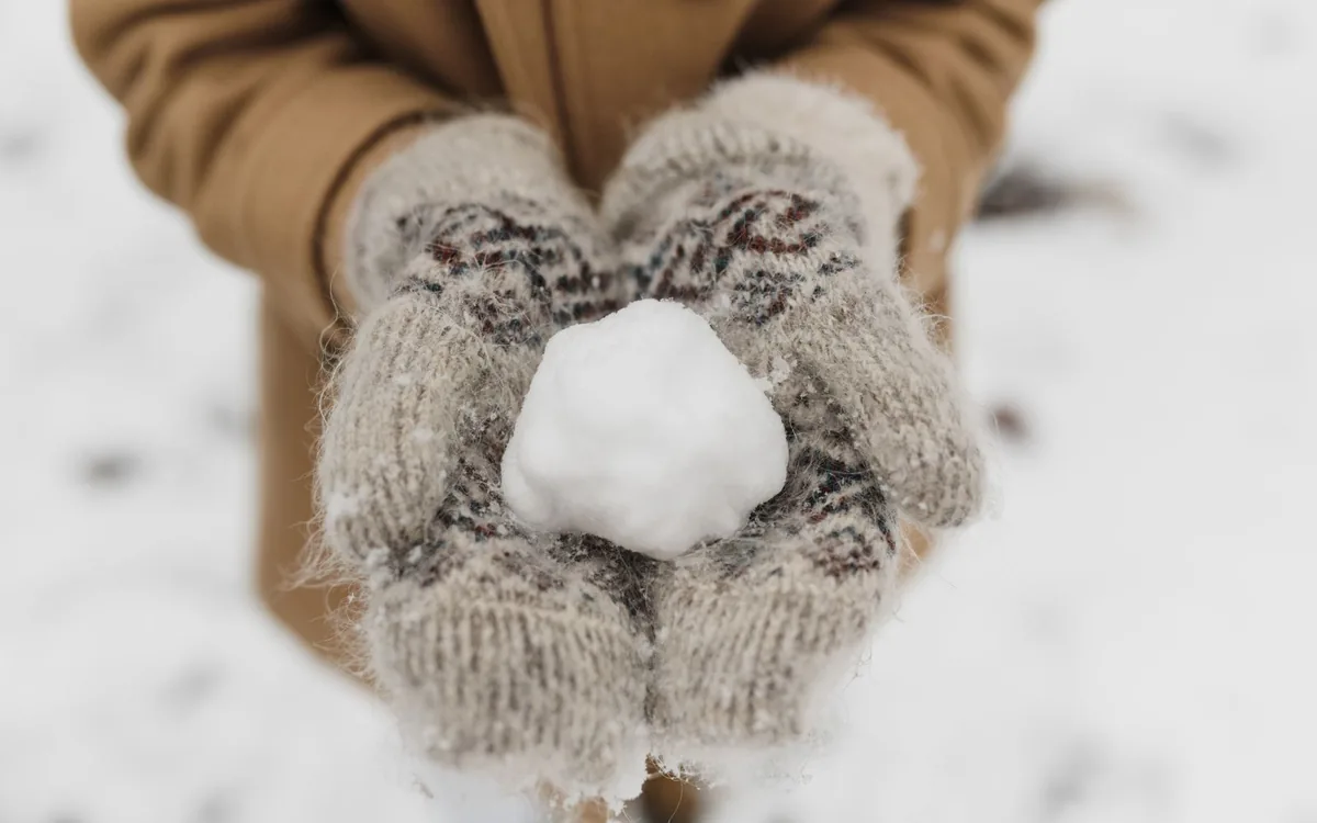 Pessoa de luvas de tricô segurando uma bola de neve entre as mãos.