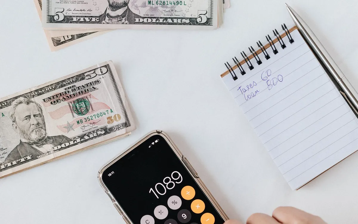 Notas de dinheiro, celular e caderno de anotações sobre uma mesa branca.