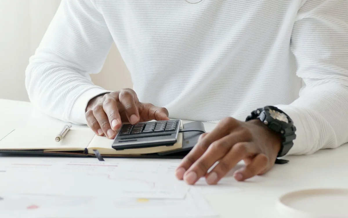 Homem digitando em uma calculadora sobre um caderno de anotações.