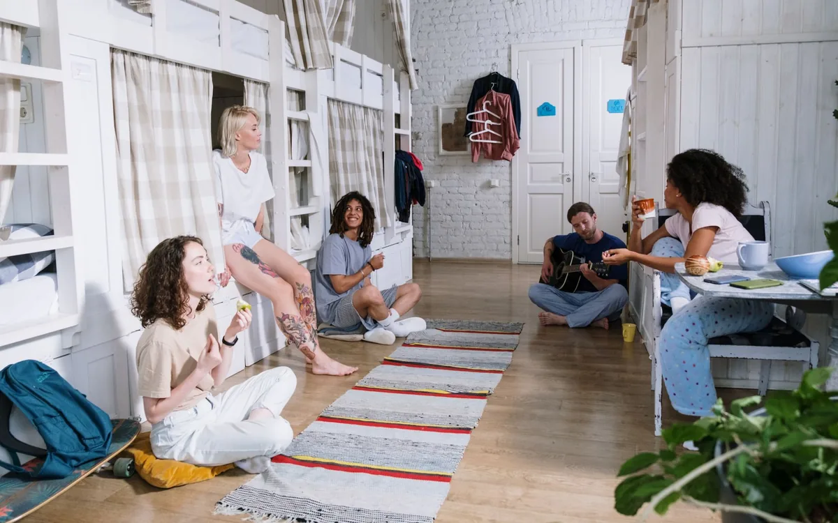 Grupo de amigos conversando em uma sala de alojamento com beliches e tapete.
