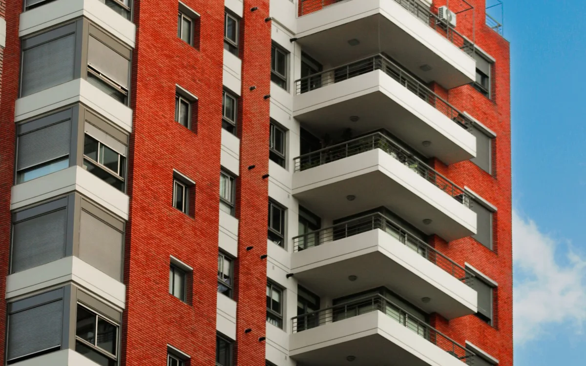 Prédio residencial de tijolos vermelhos com varandas e céu azul.
