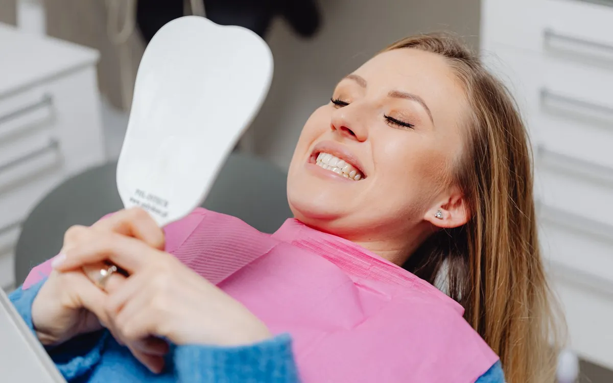 Paciente sorrindo ao se olhar no espelho na cadeira de um consultório odontológico.