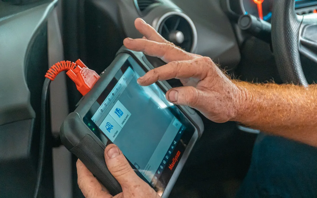 Mãos operando um aparelho de diagnóstico dentro de um carro.