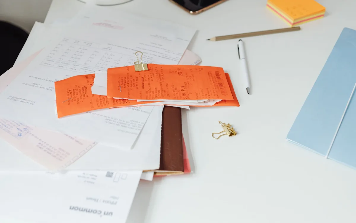 Mesa branca com recibos, notas e papéis organizados em pilhas.