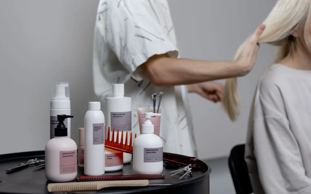 Profissional arrumando o cabelo de uma cliente ao lado de uma bancada com produtos.