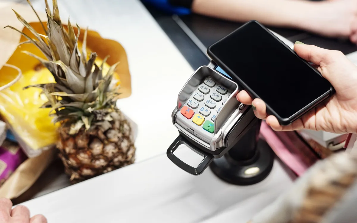 Pessoa pagando uma compra com cartão e celular no terminal.