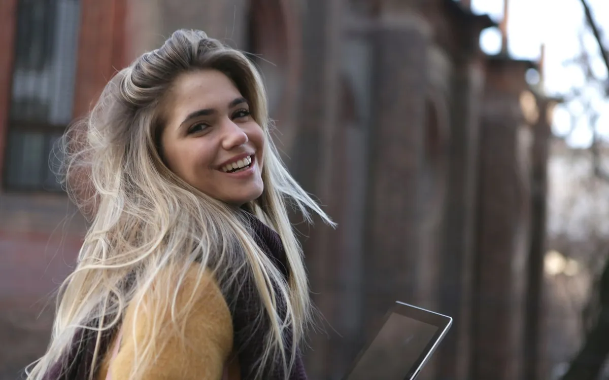 Empreendedora loira sorrindo para a câmera, segurando um tablet em uma rua.
