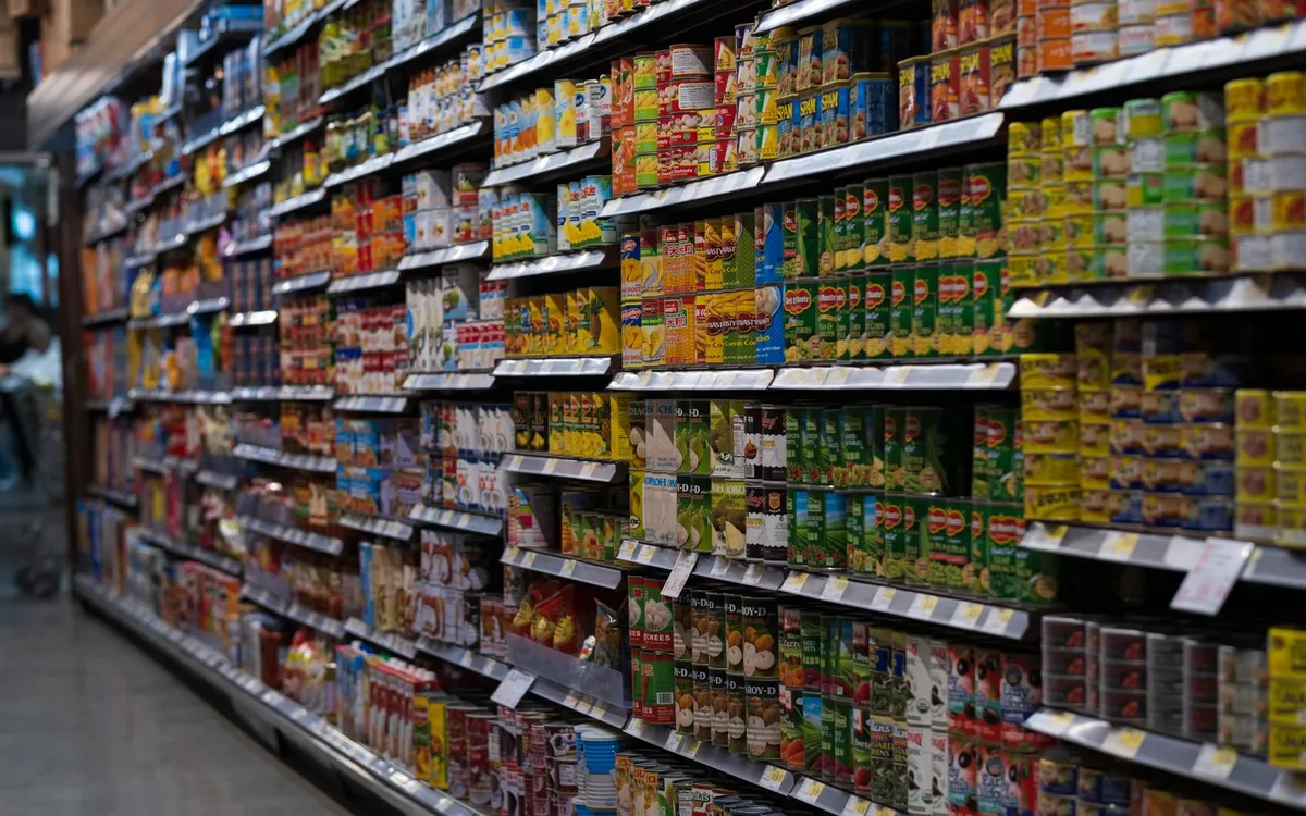 Corredor de supermercado com prateleiras repletas de produtos enlatados.