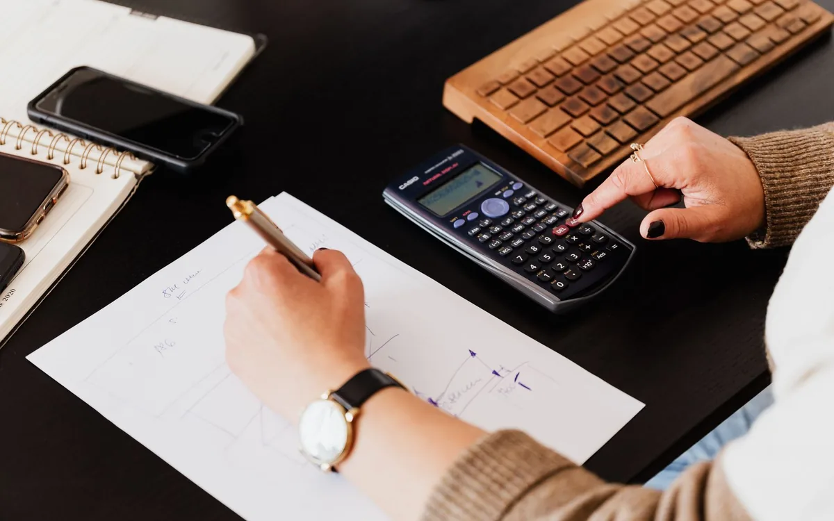 Mão usando uma calculadora sobre uma mesa.