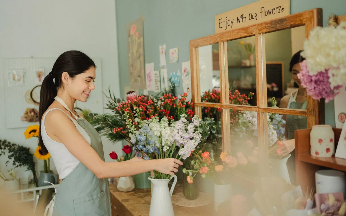 Florista de avental arrumando um buquê de flores coloridas em uma loja aconchegante.