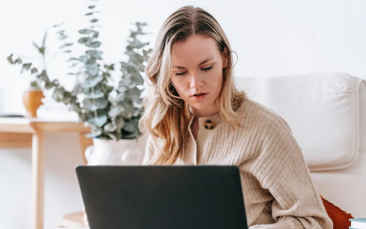 Mulher concentrada trabalhando no notebook em casa, ao lado de plantas.