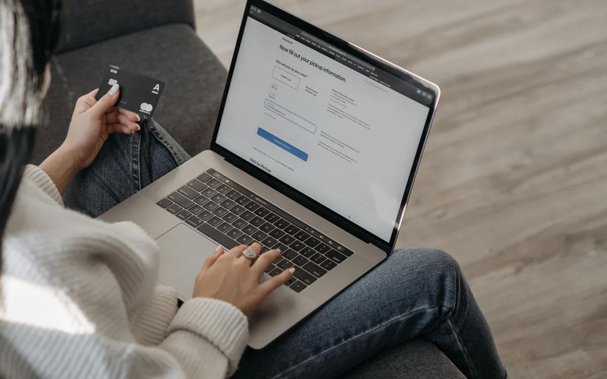 Pessoa digitando em um notebook enquanto segura um cartão de crédito.
