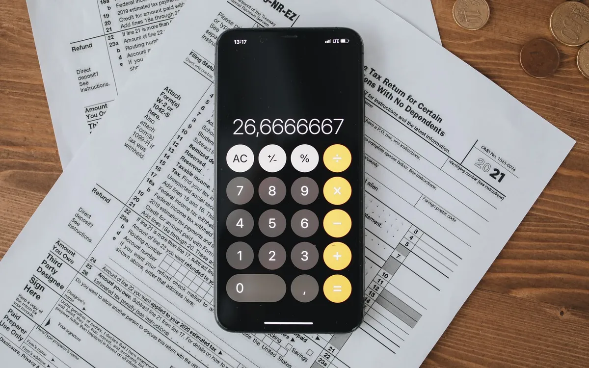 Celular com calculadora aberta sobre formulários de declaração de imposto.