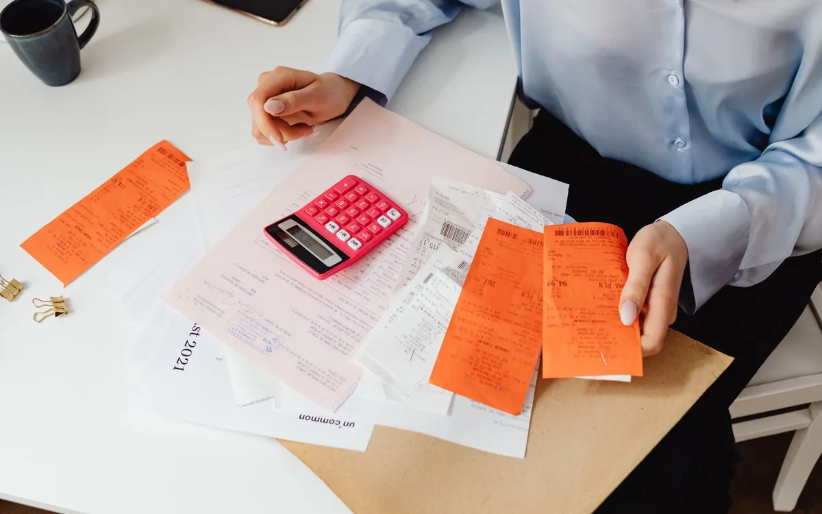 Pessoas separando recibos e notas com uma calculadora sobre a mesa.
