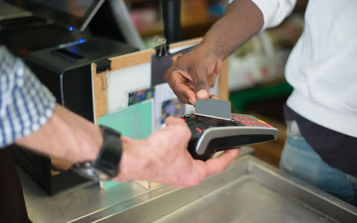Cliente aproximando o cartão da maquininha em um balcão de loja.