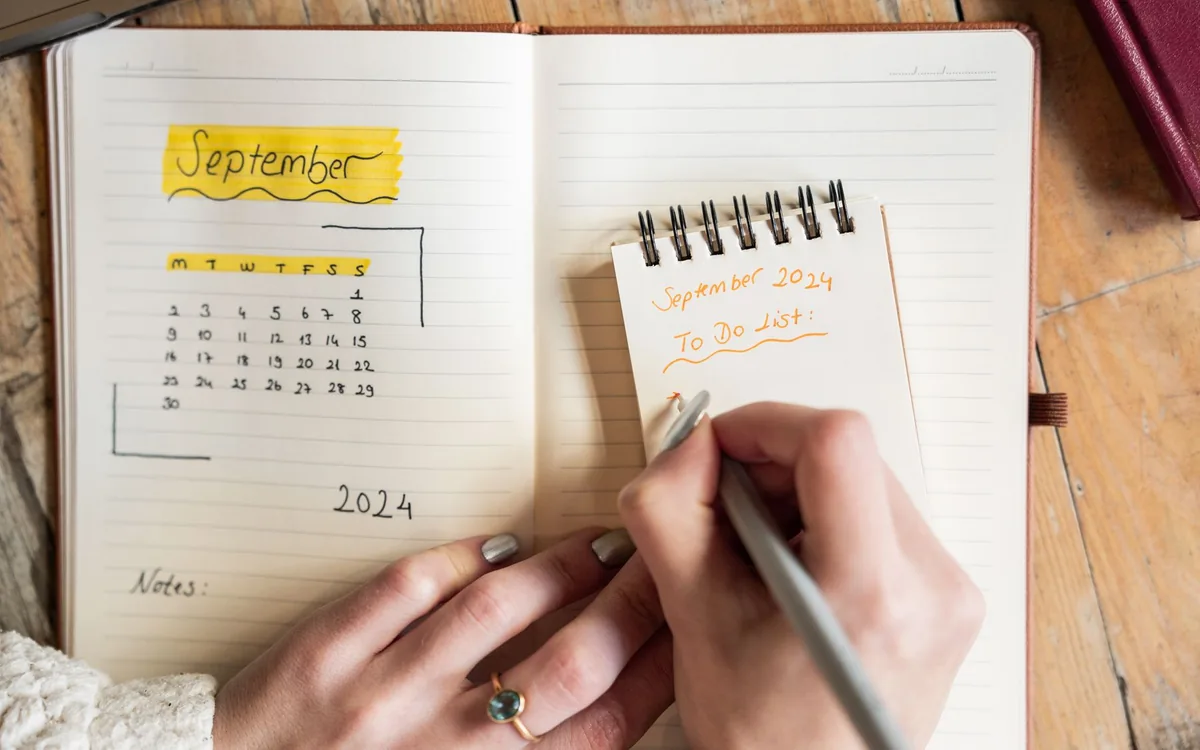 Mãos escrevendo em um caderno aberto no mês de setembro, com calendário desenhado.