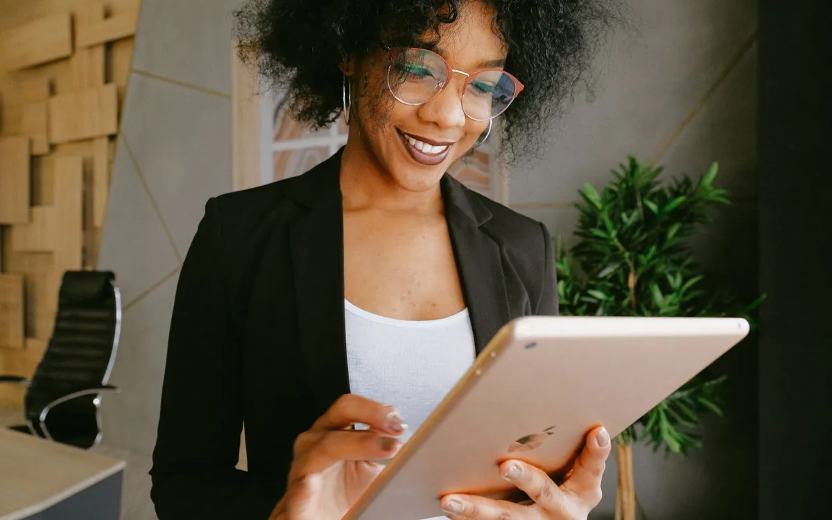 Empresária de blazer preto sorrindo e segurando um tablet.
