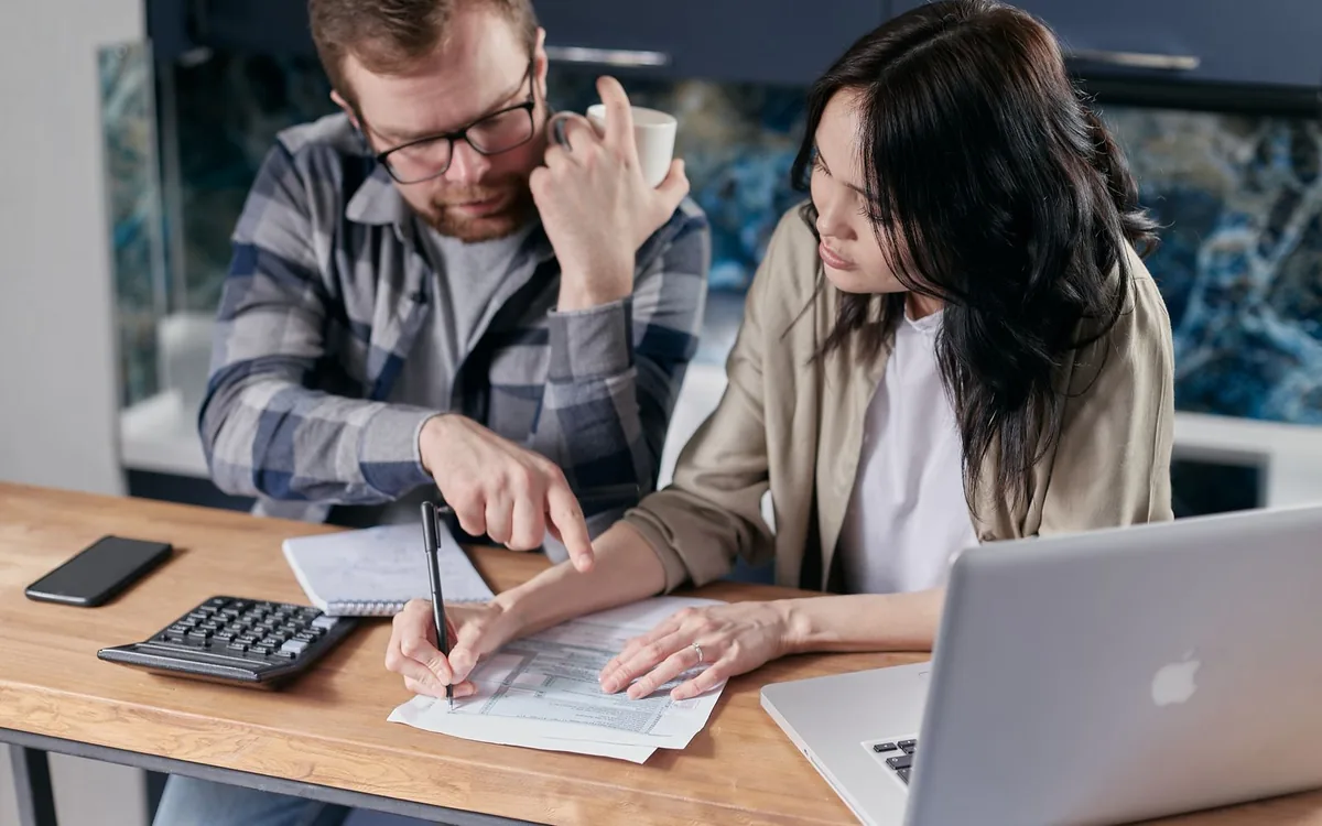 Casal à mesa com calculadora e papéis, somando as contas do mês.