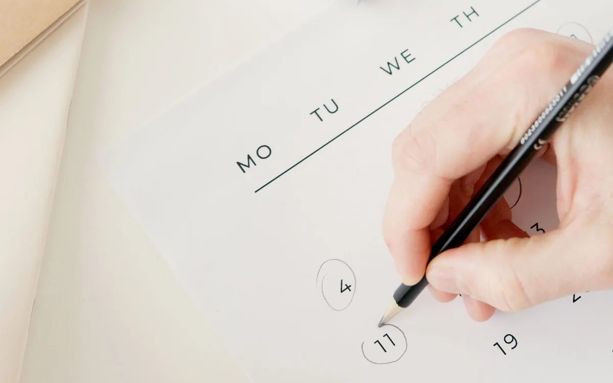 Mão desenhando um círculo em uma data de calendário com lápis.