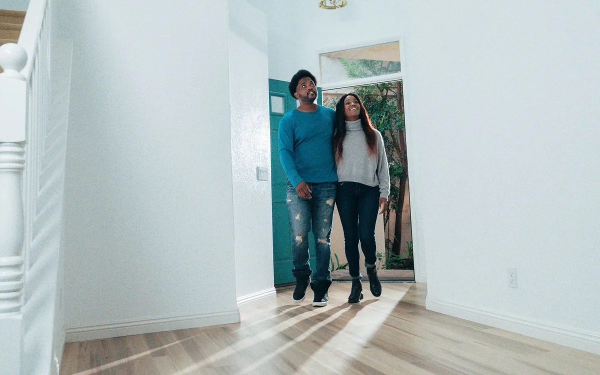 Casal entrando em um apartamento claro por um corredor, ao lado de um corretor.