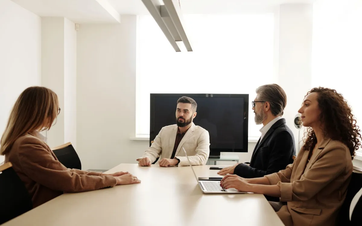 Quatro pessoas em reunião de negócios em torno de uma mesa em escritório branco.