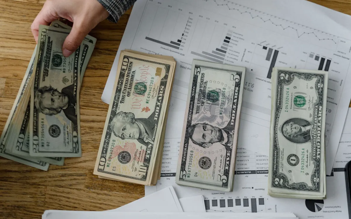 Pilhas de dinheiro em uma mesa com gráficos e relatórios financeiros.