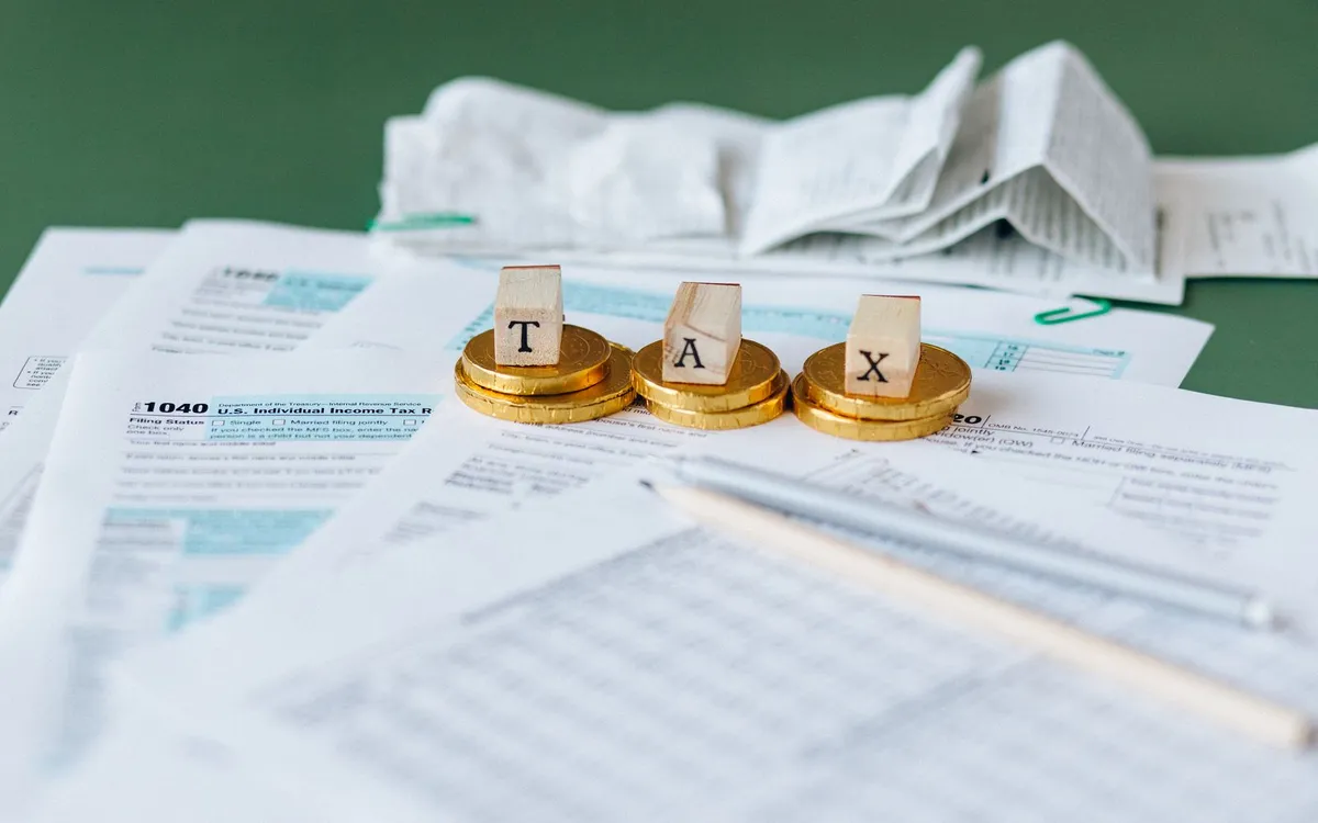 Blocos de madeira formando a palavra TAX sobre formulários de imposto.