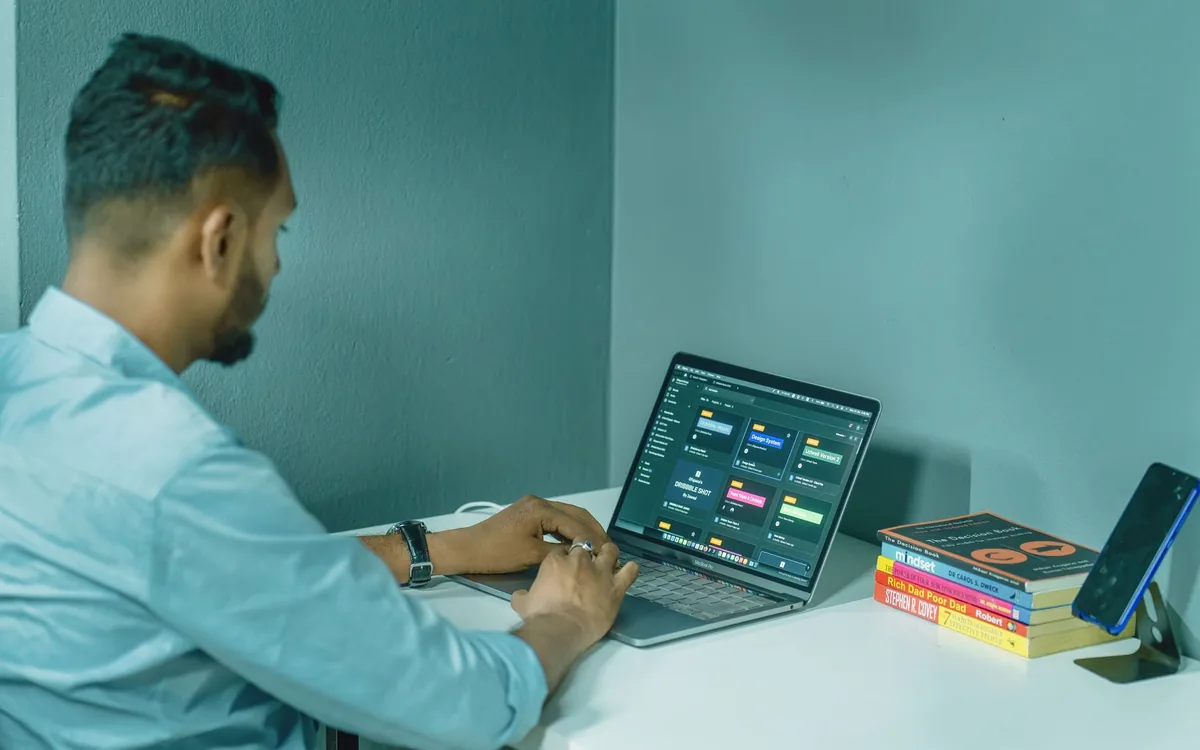 Homem trabalhando em um notebook com painel de dados em uma mesa de home office.